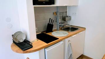 Una cocina compacta con microondas, pileta y heladera pequeña.