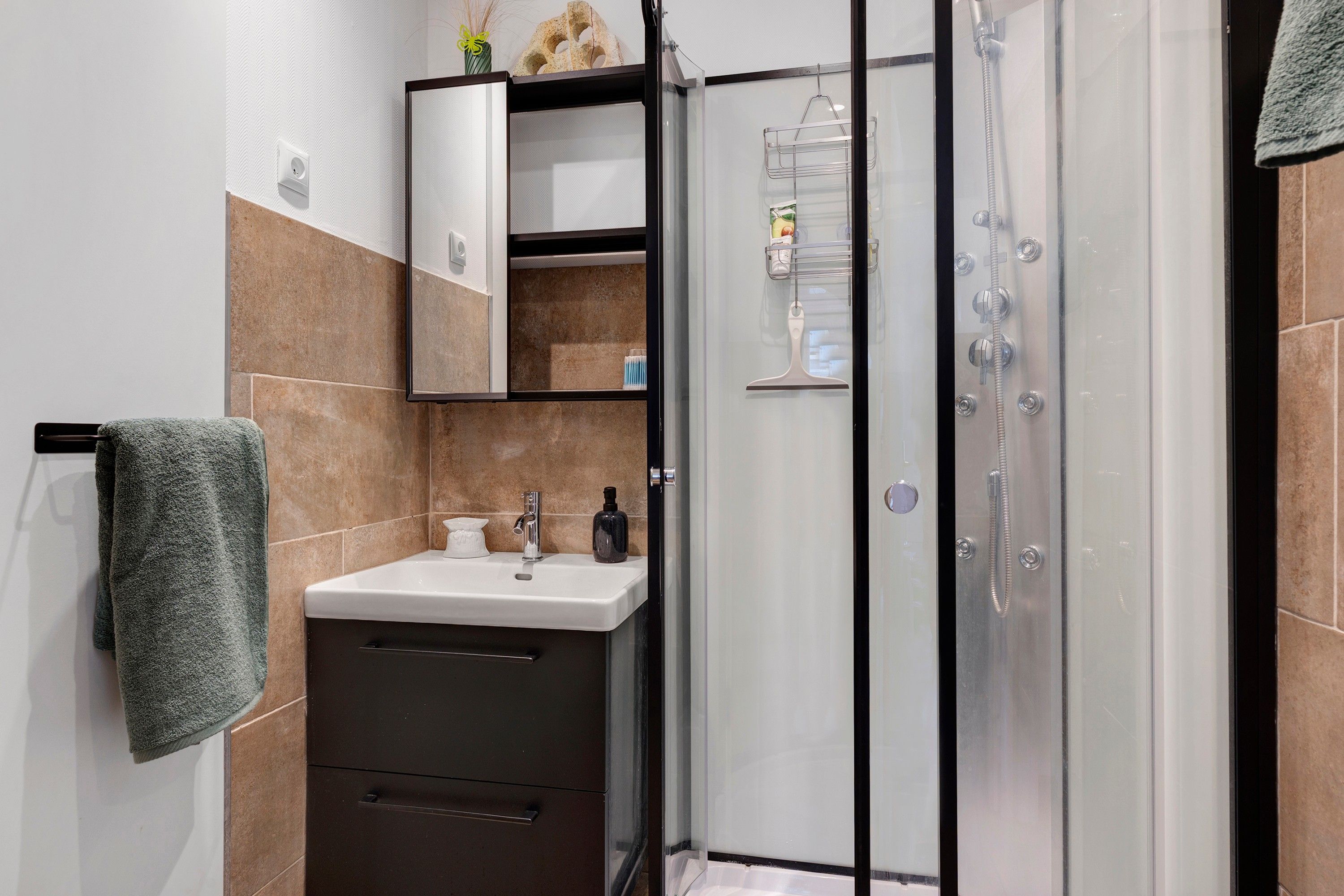 A modern bathroom with a glass shower enclosure, a sink with a mirror cabinet above, and a towel hanging on the wall.