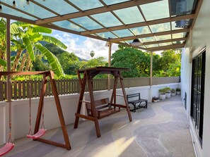 A covered outdoor area with a swing set, potted plants, and a view of greenery. - 3BR near Old Town & Chillva Market - 8 Guests (Mueang Phuket)