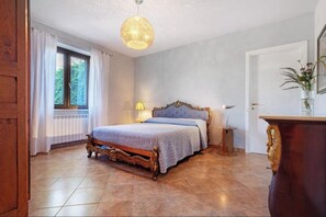 Ein Schlafzimmer mit einem hölzernen Bett, einem Nachttisch, einer Lampe und einem Fenster mit Vorhängen.