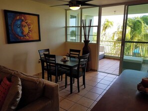 A dining area with a table and chairs, a ceiling fan, a painting on the wall, and a view of palm trees through a glass door. - Gated Complex, Pool, Balcony, Near Attractions (Boquerón)