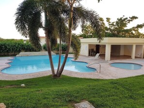 A swimming pool with two separate sections, surrounded by a grassy area and palm trees. - Gated Complex, Pool, Balcony, Near Attractions (Boquerón)