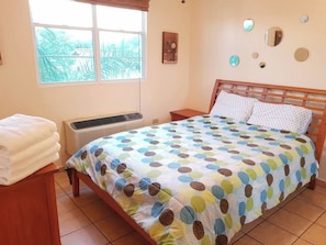A bedroom with a bed, a bedside table, a window, and a wall-mounted air conditioner. - Gated Complex, Pool, Balcony, Near Attractions (Boquerón)