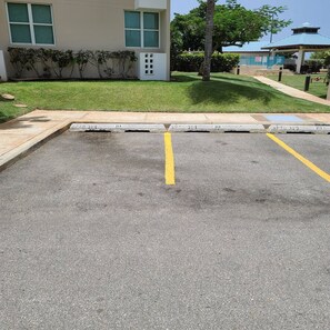A parking lot with a yellow line marking, curb cuts, and a building with windows and a covered area in the background. - Family-Friendly Stay Near Beach with Pool and BBQ (Boquerón)