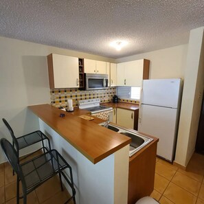 A compact kitchen with a central island, a microwave, a stove, and a refrigerator. - Family-Friendly Stay Near Beach with Pool and BBQ (Boquerón)