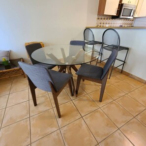 A dining area with a glass table and four chairs, a microwave above the counter, and a tiled floor. - Family-Friendly Stay Near Beach with Pool and BBQ (Boquerón)
