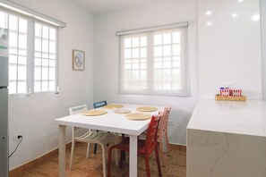 Ein Essbereich mit einem weißen Tisch, roten und blauen Stühlen und einem Fenster mit Jalousien.