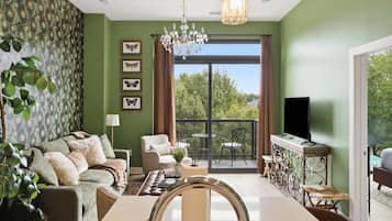 Un salon comprenant un canapé, un fauteuil, une table à manger et un balcon avec un téléviseur.