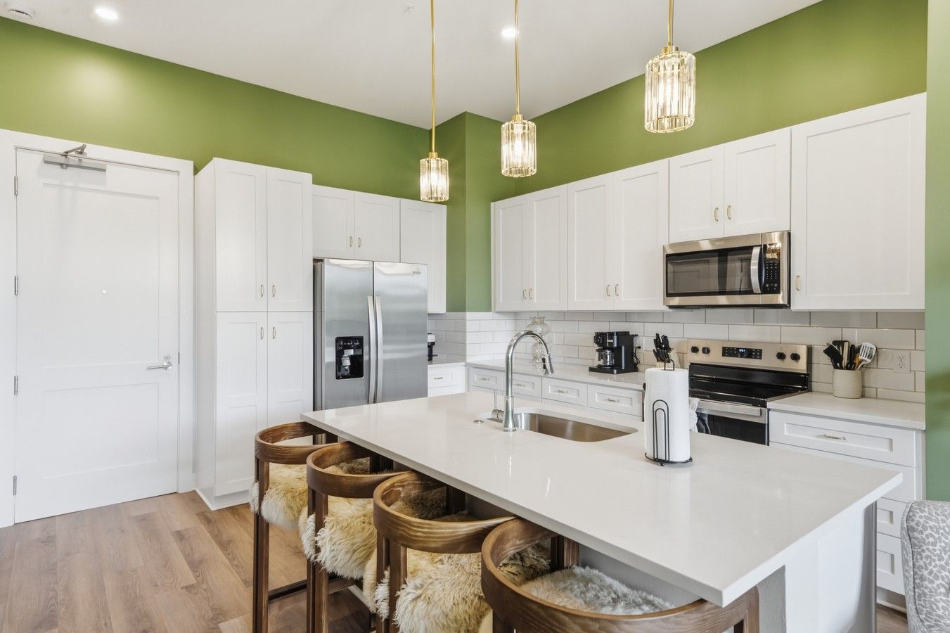 A modern kitchen with white cabinets, a stainless steel refrigerator, a microwave, and a large island with bar stools.