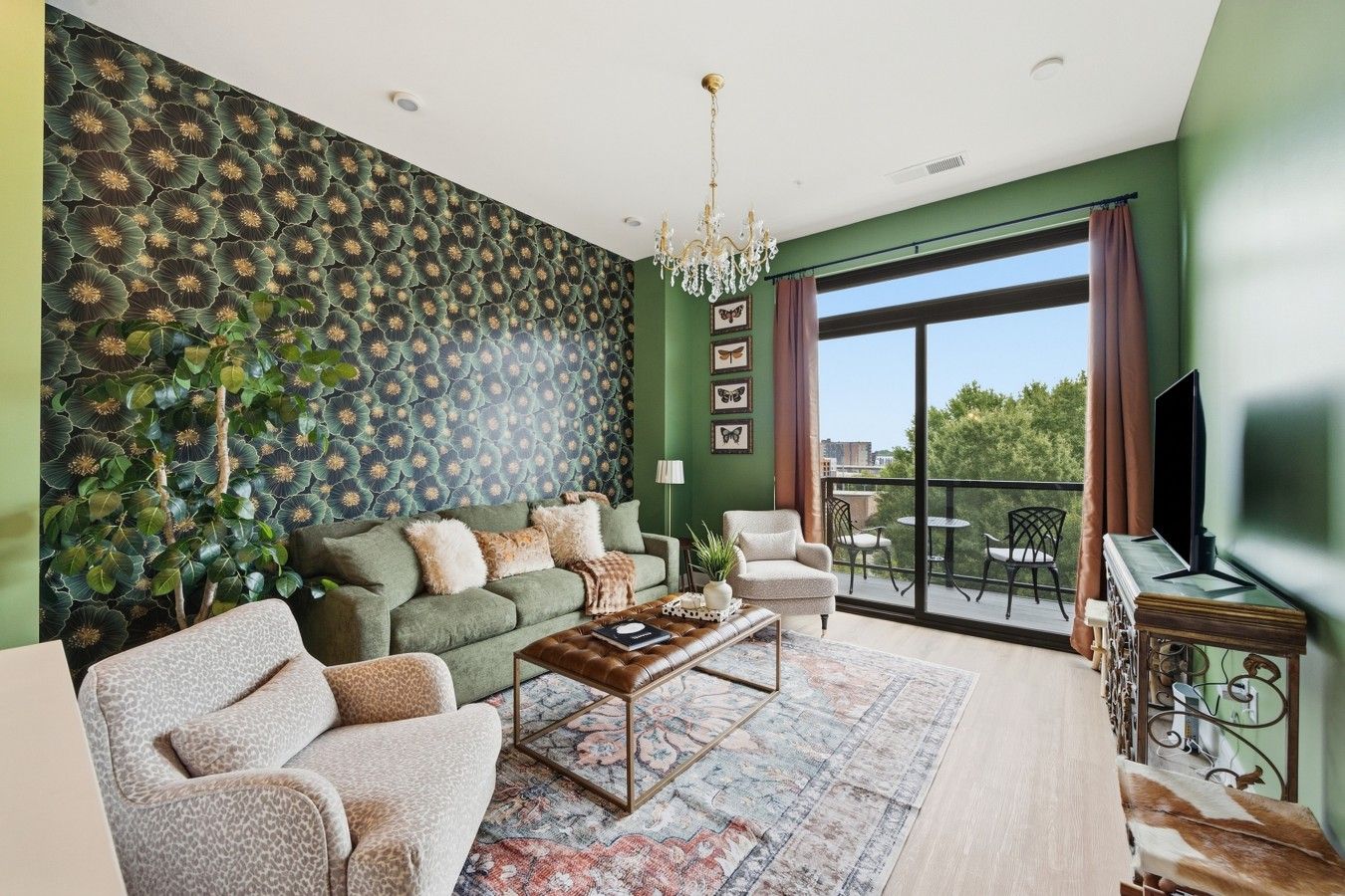 A living room with a green wall, a patterned wallpaper, a chandelier, a sofa, a coffee table, and a view of the outdoors.
