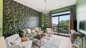 A living room with a green wall, a patterned wallpaper, a chandelier, a sofa, a coffee table, and a view of the outdoors.