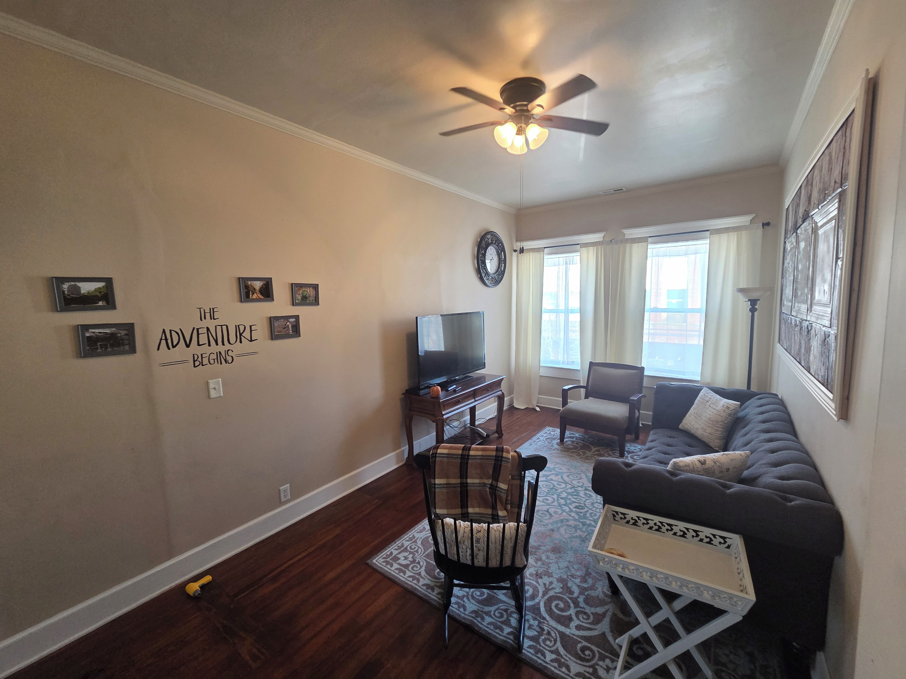 A living room with a ceiling fan, a television, a sofa, a chair, and a rug.