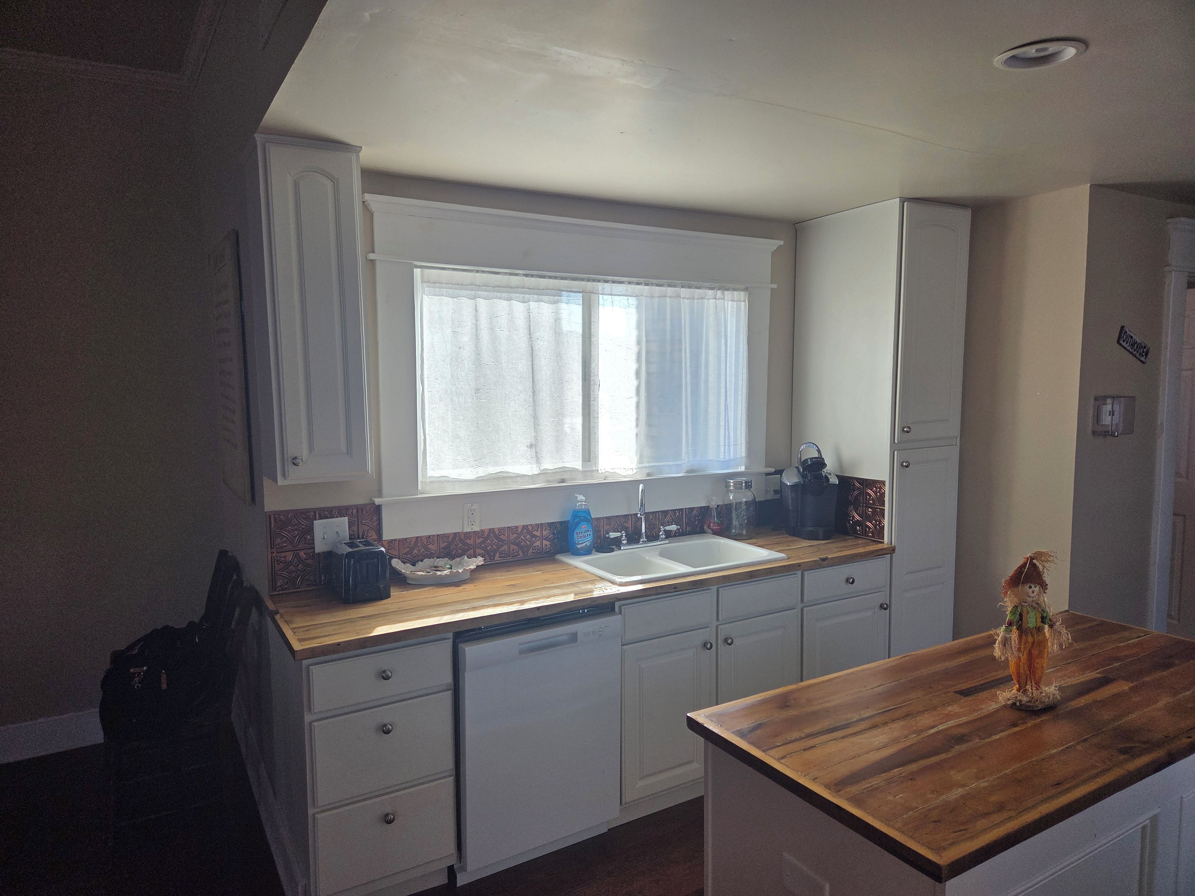 A kitchen with a window, white cabinets, a wooden countertop, and a sink.