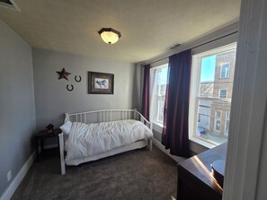 Ein Schlafzimmer mit einem Einzelbett, einem Nachttisch, einem gerahmten Bild, einer Stern-Dekoration und einem Fenster mit Vorhängen.