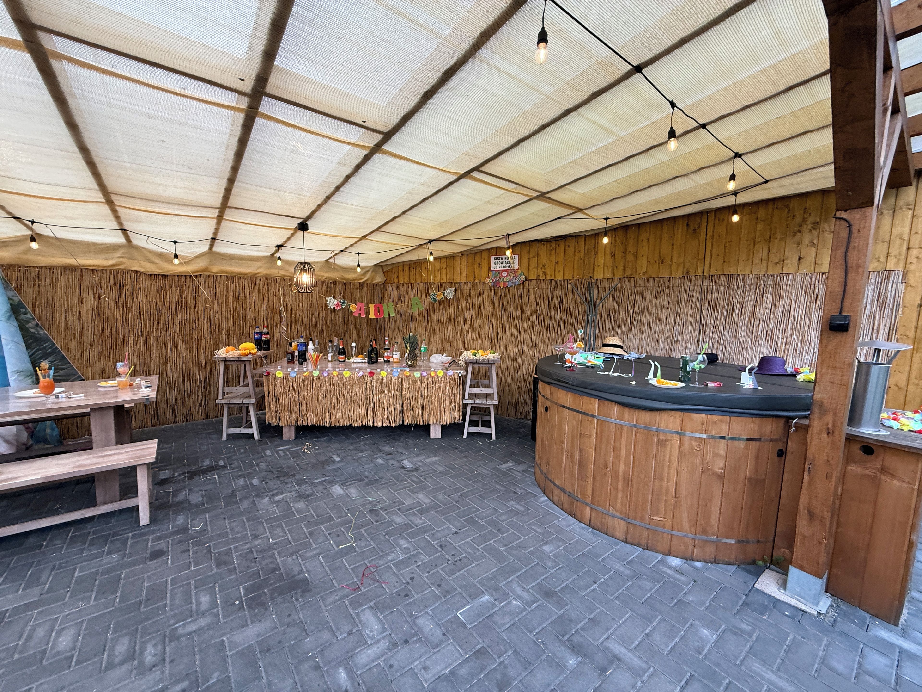 An indoor venue with a brick floor, wooden walls, a central bar area, and string lights.