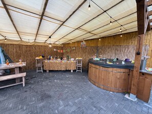 An indoor venue with a brick floor, wooden walls, a central bar area, and string lights.