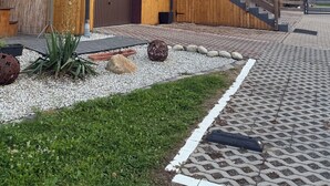 En træbygning med garage, trappe og en belagt område med planter og sten.
