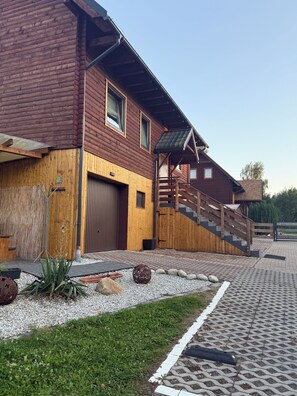 Ein Holzhaus mit Garage, einer Treppe und einer bepflasterten Fläche mit Pflanzen und Steinen.