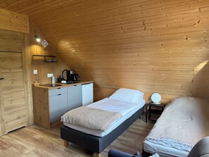 Ein kleines Zimmer mit Bett, Nachttisch und einer Küchenzeile.