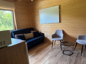 A wooden interior with a sofa, two armchairs, a small table, and a whiteboard on the wall.