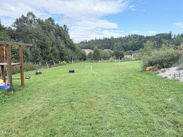 A grassy outdoor area with a wooden structure, possibly a play area, and a soccer goal.