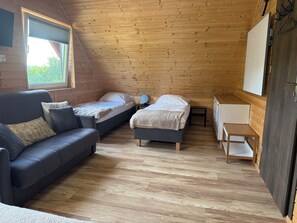 A cozy room with a wooden ceiling, a sofa, two beds, a small table, and a TV.