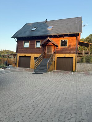 A wooden house with a sloped roof, a front porch, and two garage doors.
