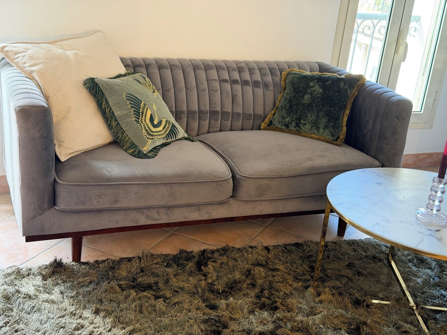 A grey upholstered sofa with a tufted backrest, a round marble coffee table, and a shaggy rug.