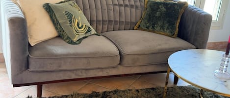 A grey upholstered sofa with a tufted backrest, a round marble coffee table, and a shaggy rug.