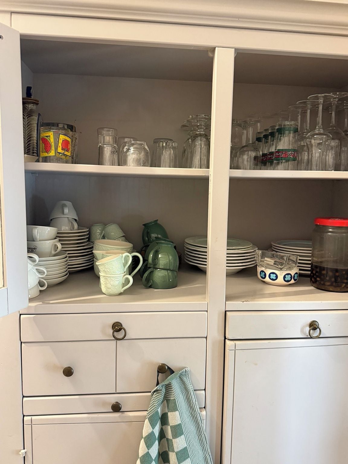 Un armario de cocina con repisas que contienen cristalería, platos y frascos.