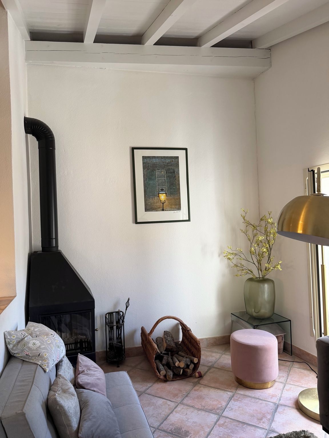 Un salon chaleureux avec une cheminée, un tableau encadré, une lampe et un vase rempli de fleurs.