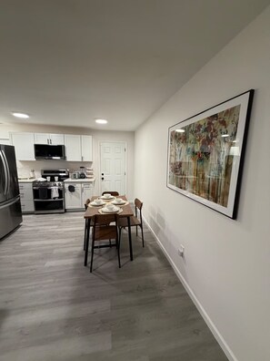 A modern kitchen with white cabinets, a dining table set for four, and a large abstract painting on the wall. - Cozy 2 Bedroom Near Uptown, Dining & Fun (Charlotte)