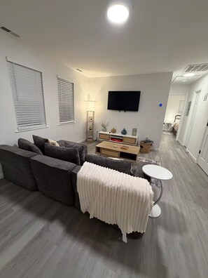 A living room with a grey sofa, a coffee table, and a TV mounted on the wall. - Cozy 2 Bedroom Near Uptown, Dining & Fun (Charlotte)
