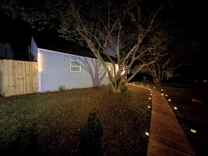 A house with a tree in the yard, a wooden fence, and a pathway with lights. - Cozy 2 Bedroom Near Uptown, Dining & Fun (Charlotte)