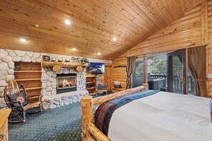 A log cabin room with a stone fireplace, a bed, a rocking chair, and a television. - Private Hot Tub | Walk to the Resort (Park City)