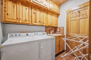 Een wasruimte met een wasmachine en droger, houten kastjes en een droogrek.