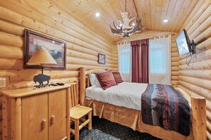 Een blokhutkamer met een bed, een bureau, een lamp, een bevestigde televisie en een plafondlamp.