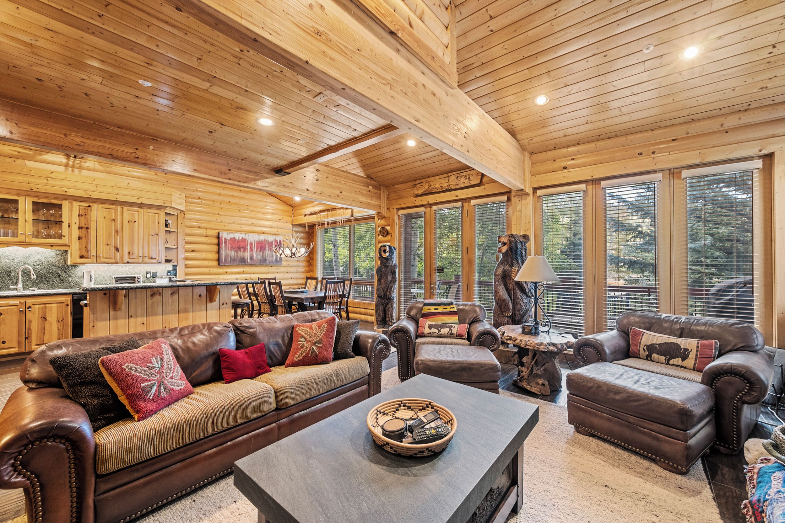 A log cabin interior with a dining area, leather sofas, and a fireplace.