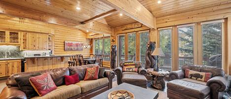 A log cabin interior with a dining area, leather sofas, and a fireplace.