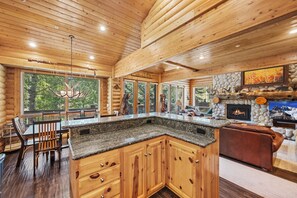 A spacious log cabin interior with a large kitchen island, dining area, and a stone fireplace. - Private Hot Tub | Walk to the Resort (Park City)