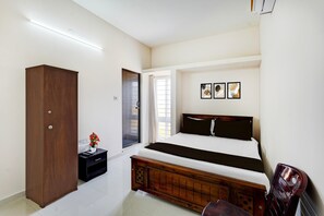 A bedroom with a bed, a wardrobe, a bedside table with a vase, and a window with curtains. - Super Collection O Sholinganallur (Chennai)