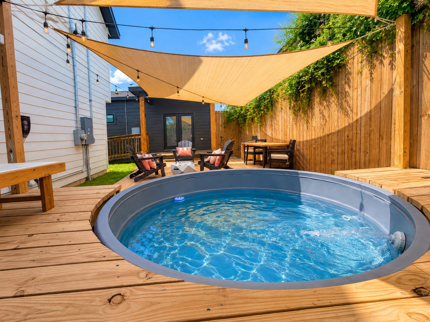A hot tub on a wooden deck with a wooden fence and a house in the background.