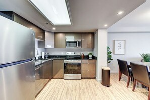 A modern kitchen with stainless steel appliances, wooden cabinets, and a dining area with a table and chairs. - The Skyside | 27th Floor | Penthouse + City Views (Saskatoon)