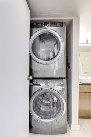A compact, two-door wall-mounted washing machine in a small laundry room. - The Skyside | 27th Floor | Penthouse + City Views (Saskatoon)