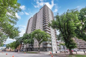 A multi-story residential building with balconies, surrounded by trees and parked cars. - THE COSMOPOLITAN- YXE Penthouse (Saskatoon)