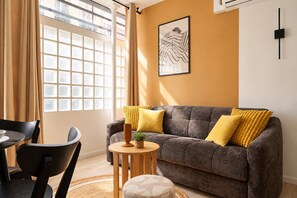 A living room with a sofa, a small round table, a chair, and a window with curtains. - TheBlueStay 365 - Beautiful A/C Apartment in Paris (Paris)
