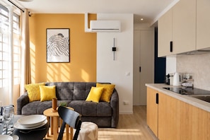 A modern living room with a sofa, a dining table with chairs, and a kitchen area with a countertop and cabinets. - TheBlueStay 365 - Beautiful A/C Apartment in Paris (Paris)