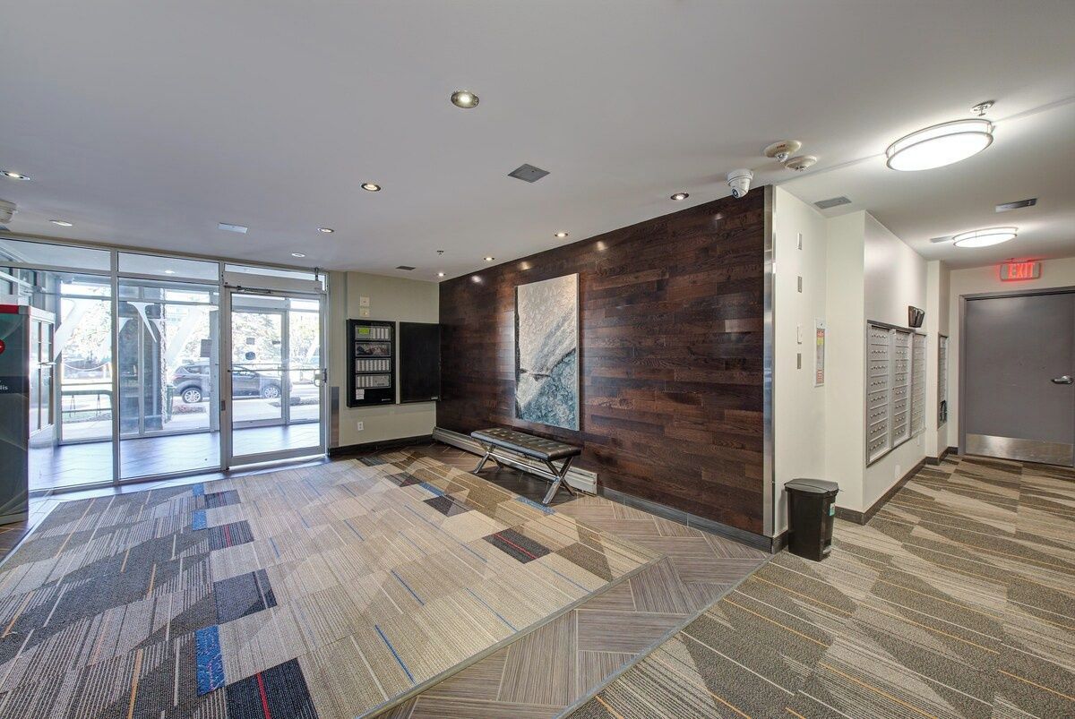 A hotel lobby with a patterned carpet, a bench, a wall-mounted artwork, and a reception desk.