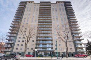 A multi-story residential building with balconies, a ground-level entrance, and a parking area. - The Bruno - 1 BR - Close to RUH (Saskatoon)