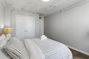 Ein Schlafzimmer mit einem Bett, einem Nachttisch, einer Lampe, einem Kleiderschrank und einem Stapel gefalteter Handtücher.